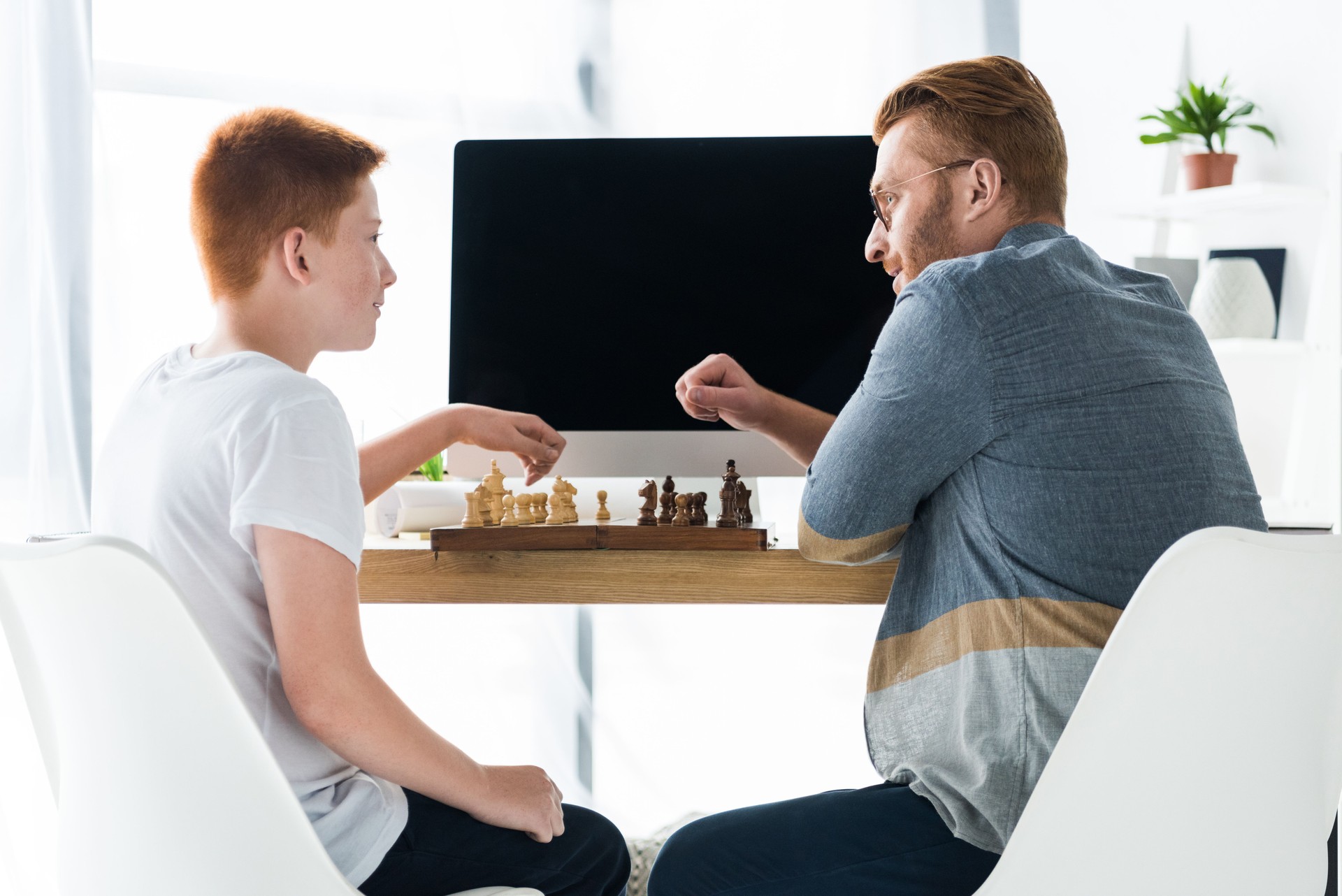 side view of father and son playing chess at home