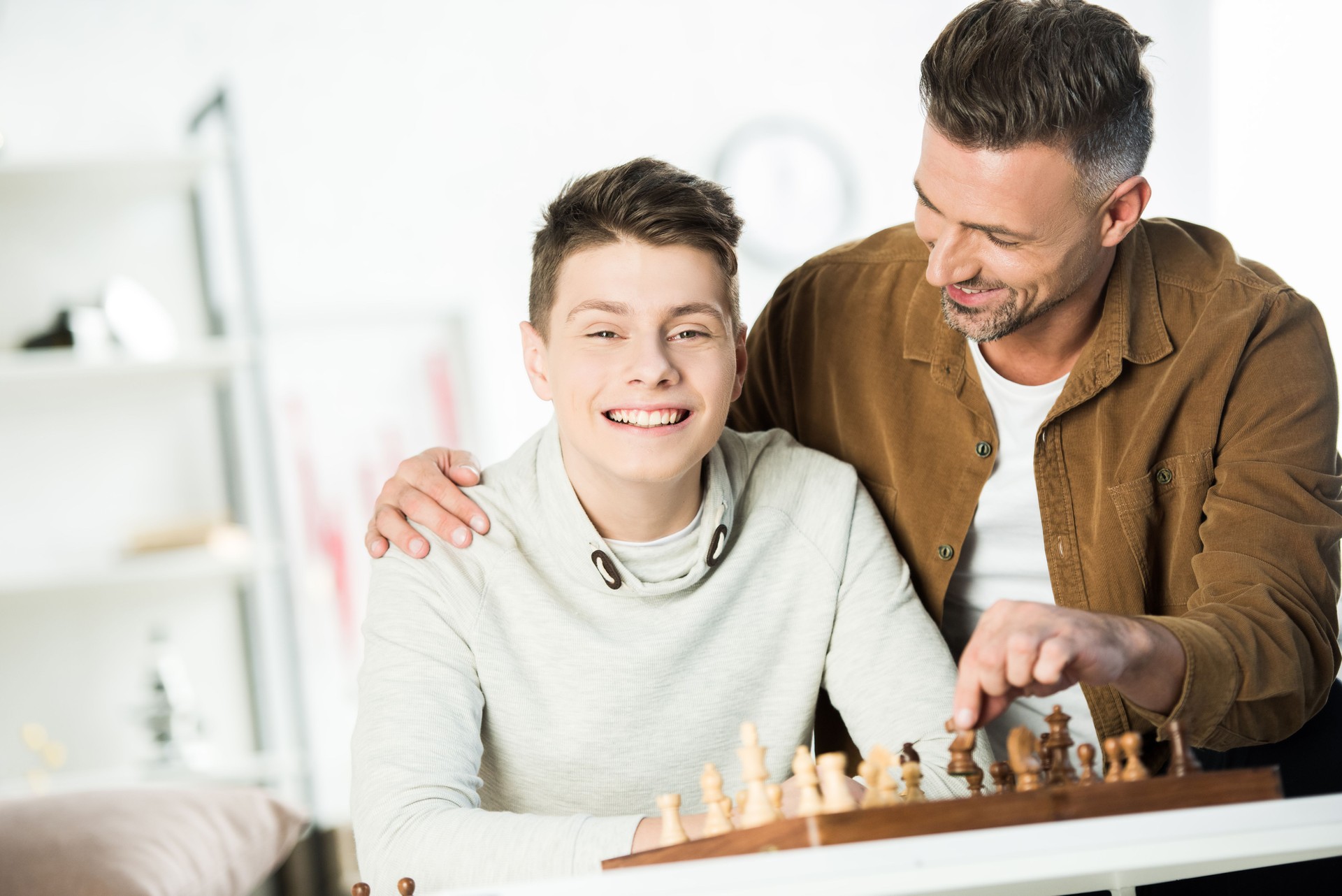 father hugging happy teen son at table with chess at home