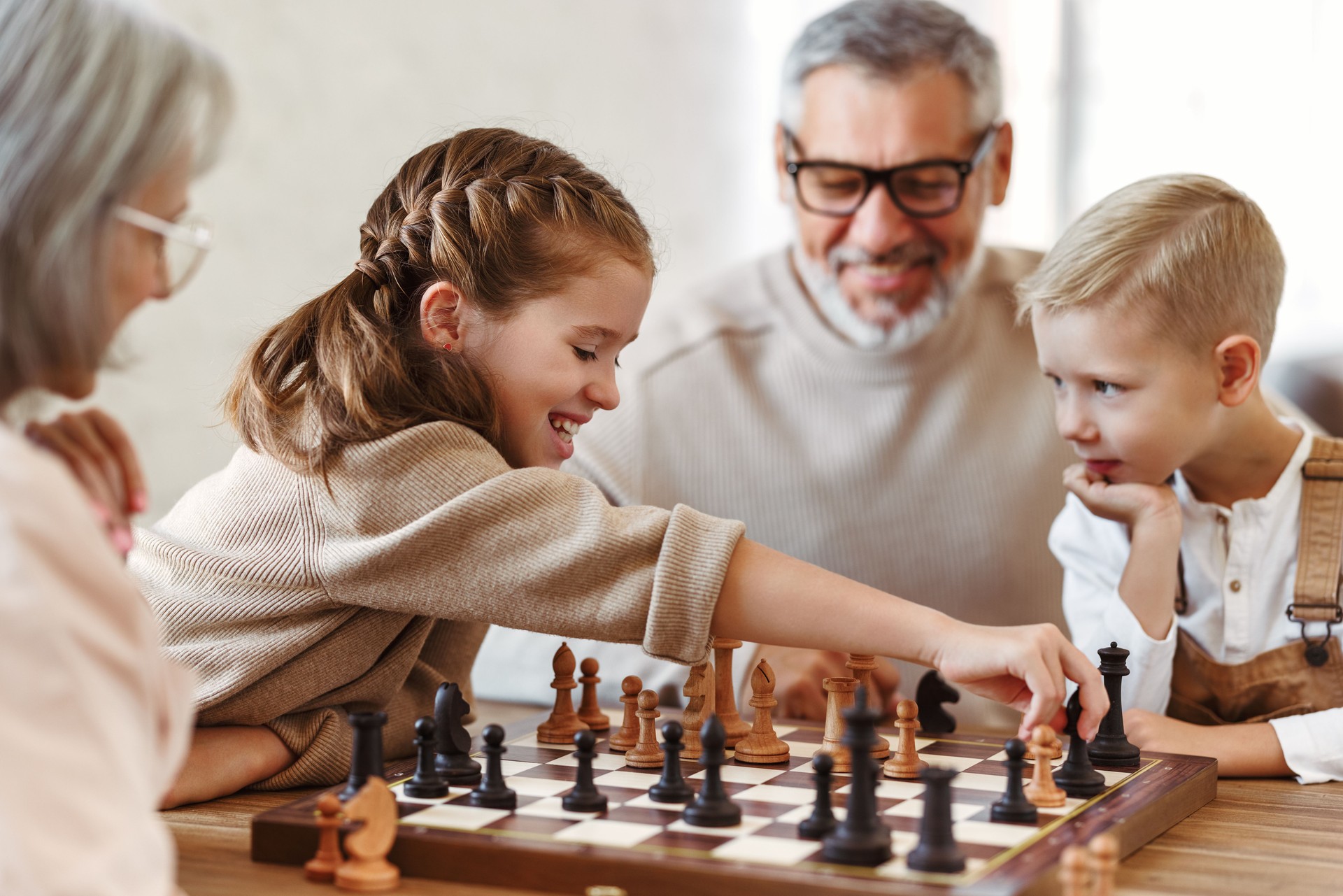 Children brother and sister playing chess while sitting in living room with senior grandparents